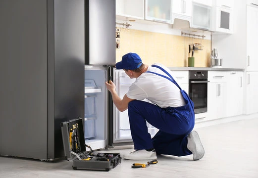 Technician inspecting a stainless steel refrigerator with tools nearby