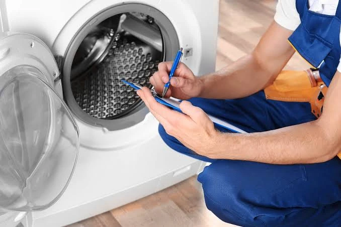 Technician writing diagnostic notes beside an open front-loading washer